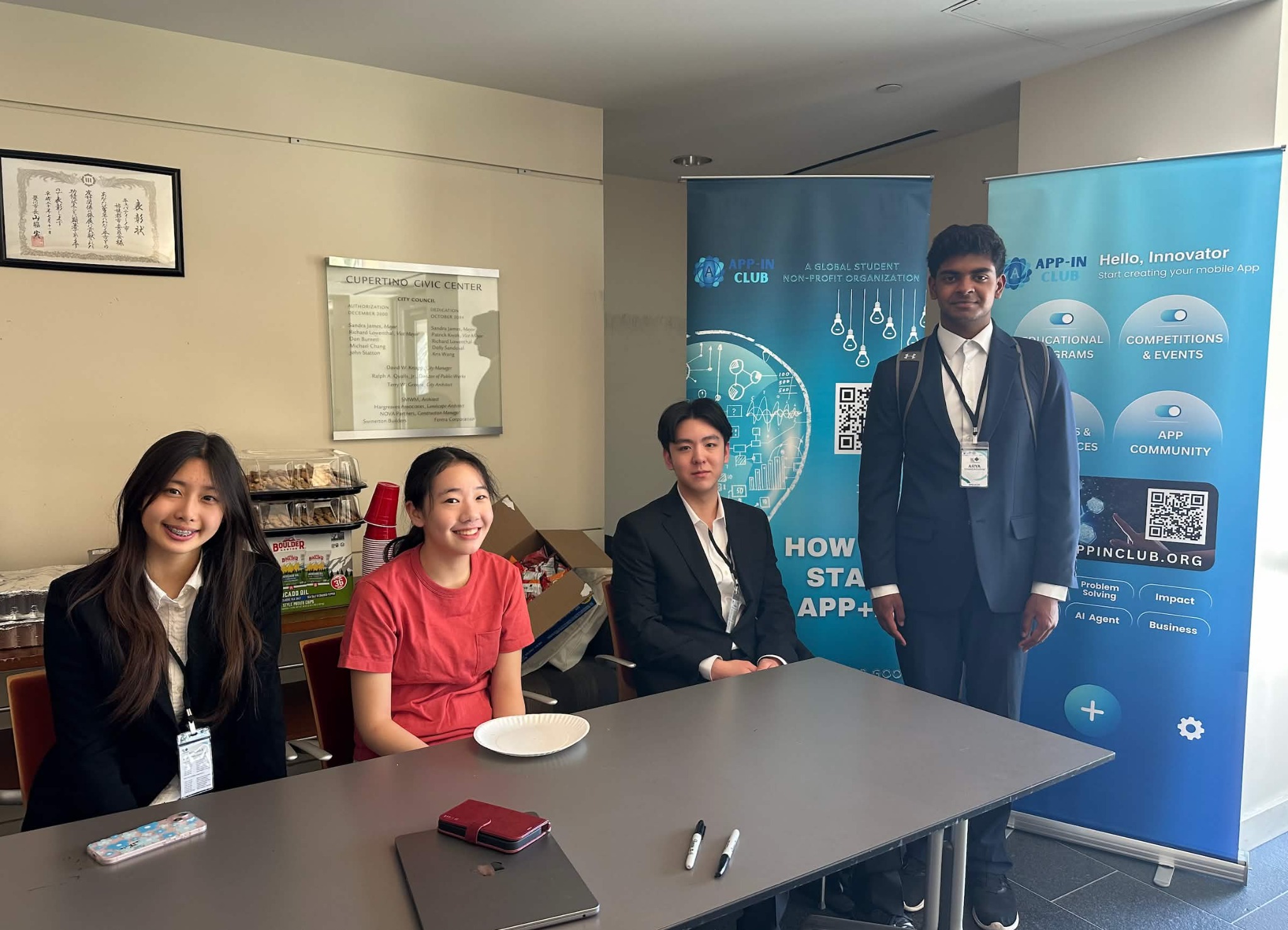 Four App-In Club officers gathered at a table in front of the club’s banners