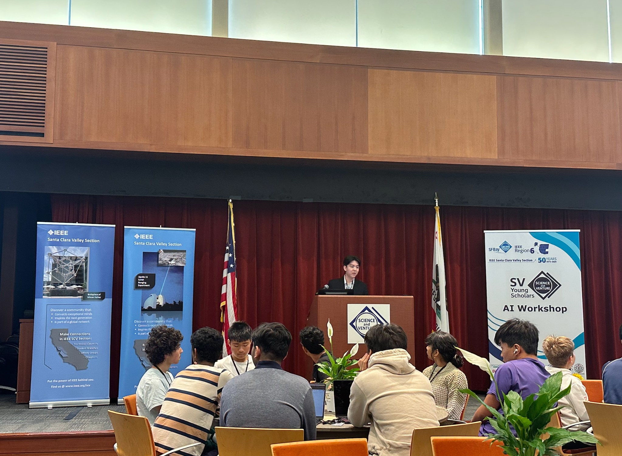 A presenter addressing workshop participants beside IEEE and SV Young Scholars banners